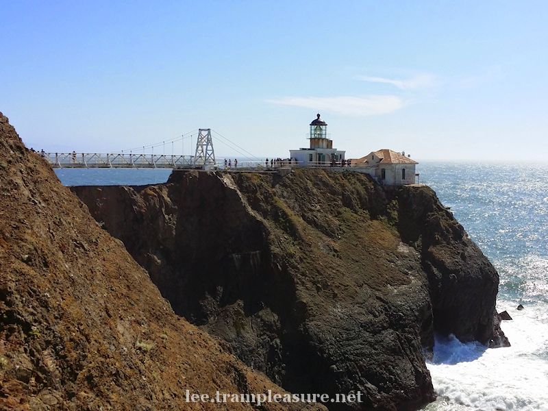 photo showing a footbridge leading out to a lighthouse on a cliff over the ocean