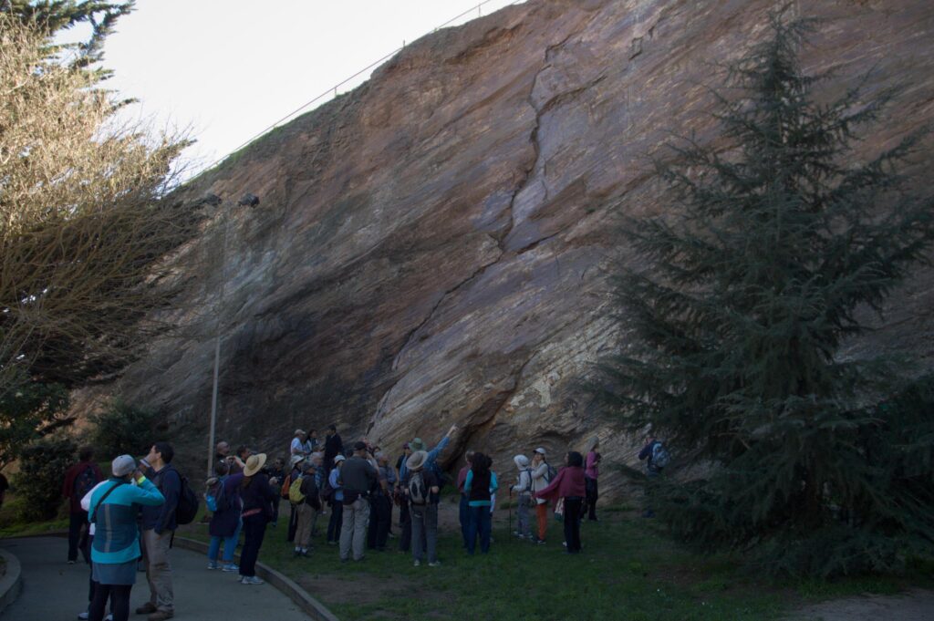 photos showing a group of people in front of a rock cliff with slick sides.